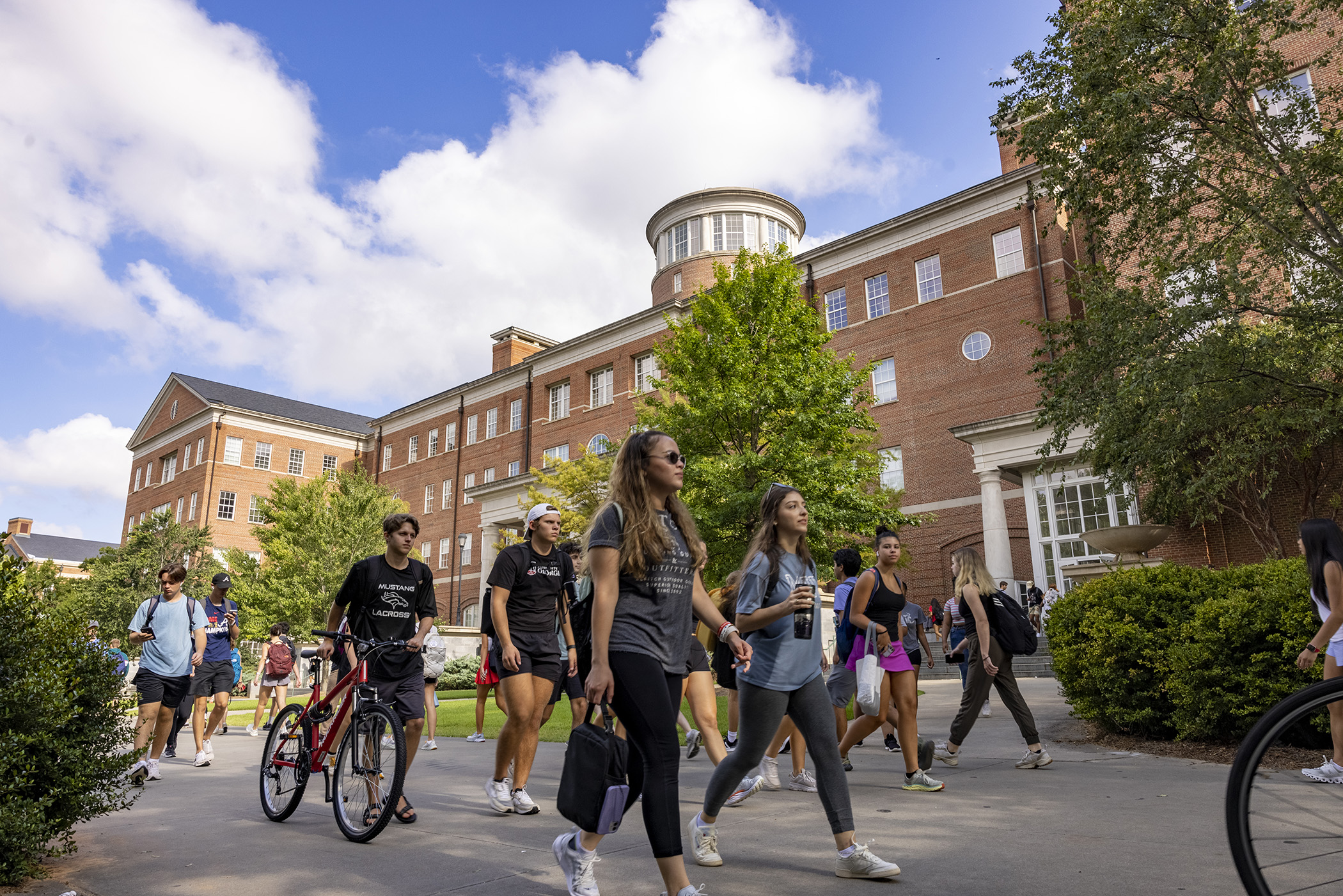 View of students walking on the sidewalk in front of the Miller Learning Center on a sunny summer day.